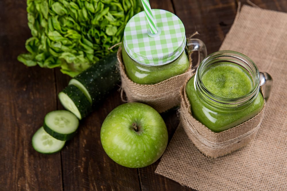 The health benefits of Juicing-Delicious Juice, jars with green juice, apple and cucumber, lettuce beside the jars