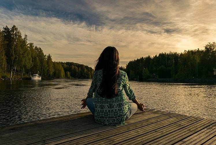 a woman meditating near a lake