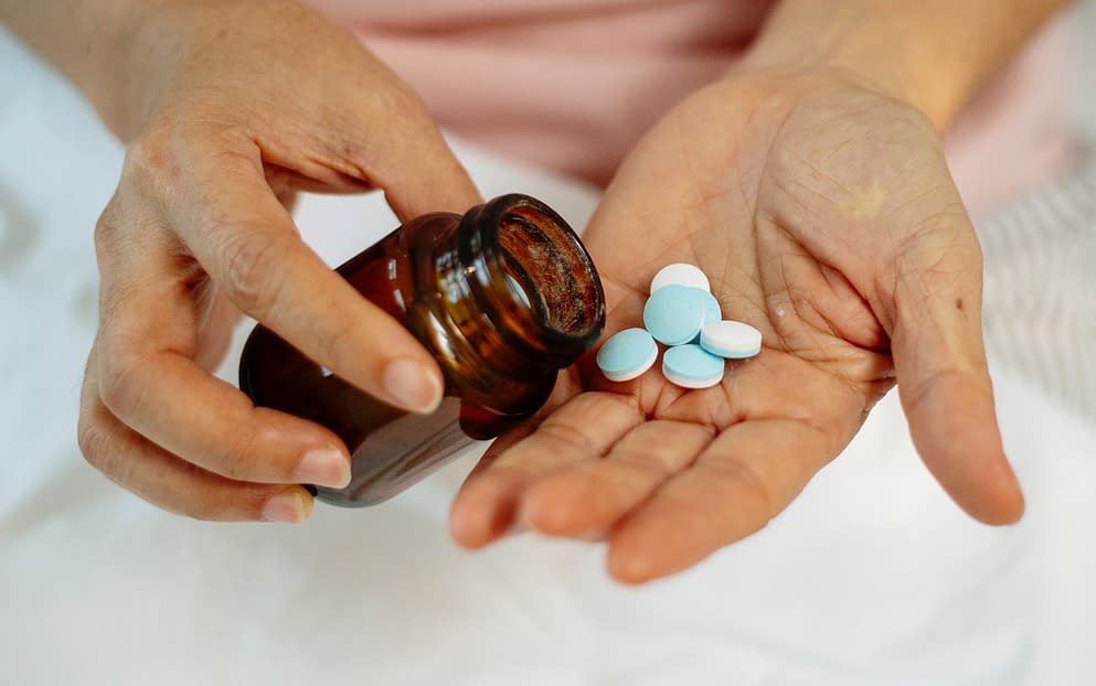 someone takes blue-colored tablets out a brown bottle in her hands