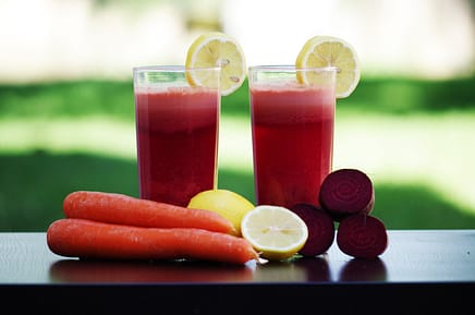 two glasses of juice, two carrots, lemons and beet root beside the glasses