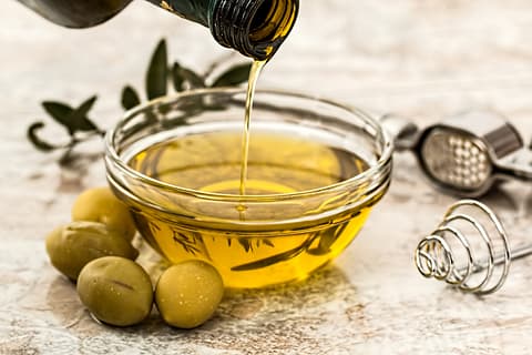 olive oil in a bowl and green olives beside the bowl