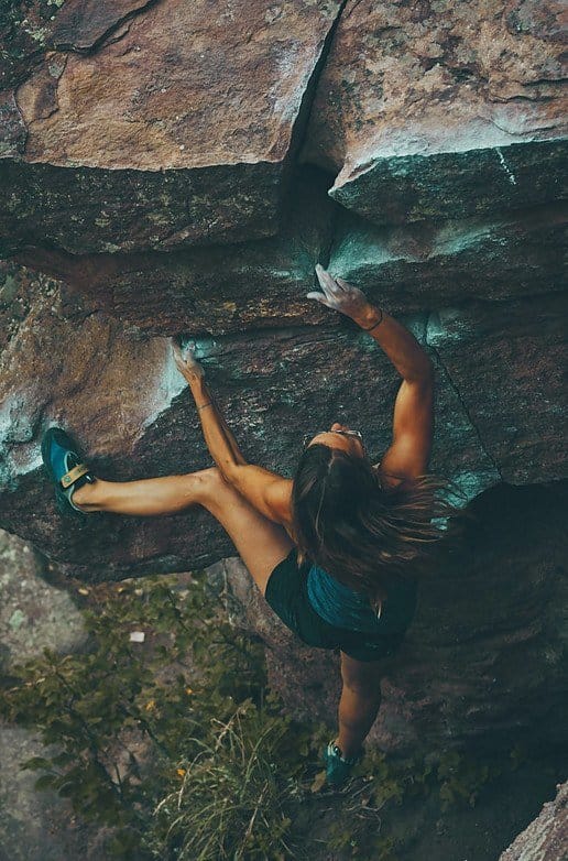 a woman with black hair is doing freeclimbing in a wall of a mountain