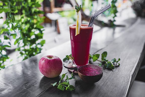 beet and apple juice in a glass with a straw on a table, beside an apple a beetroot