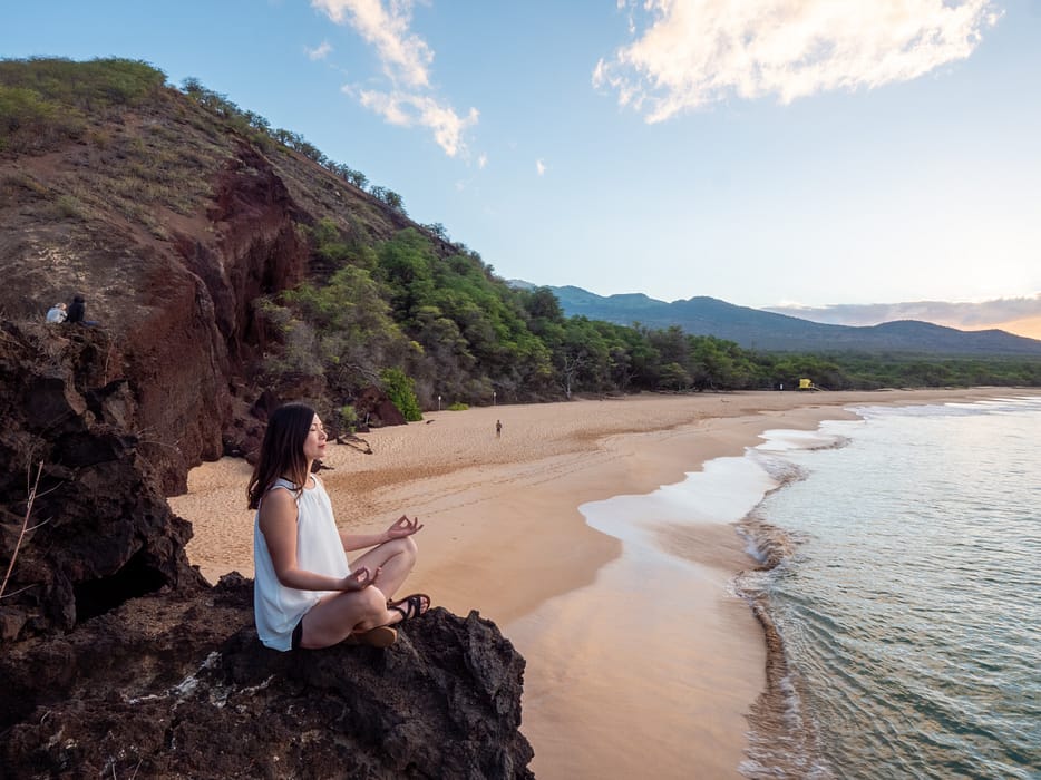 woman meditating on a rock at the beach