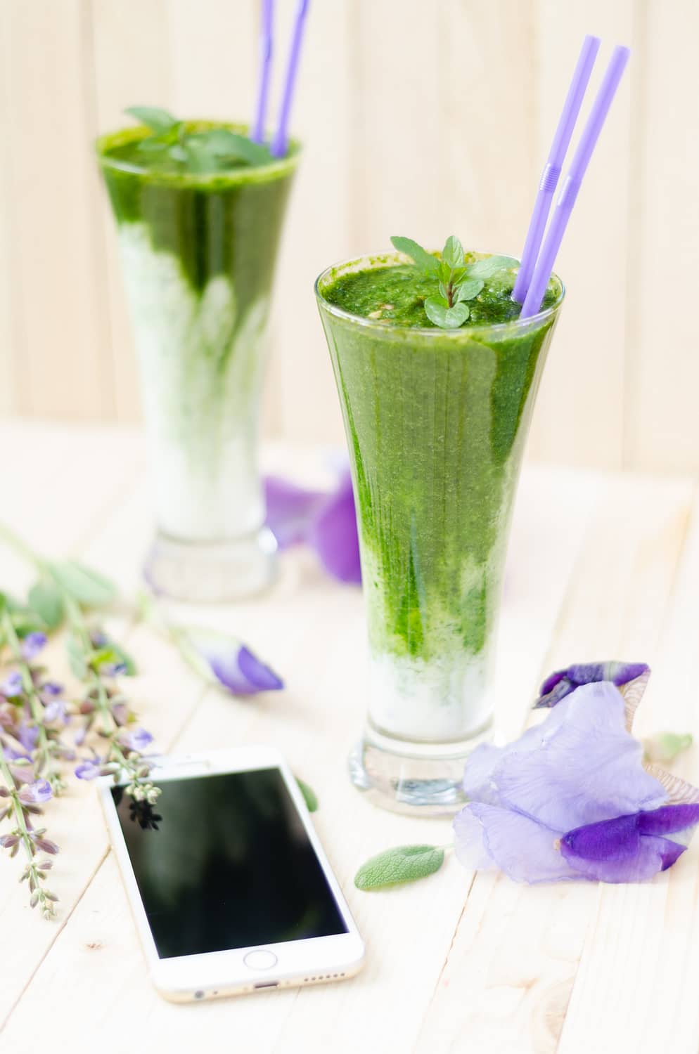 green juices in two glasses with two straws a mobile phone in the front